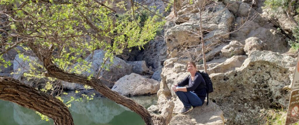 Marjorie sits among huge rocks next to a pond.