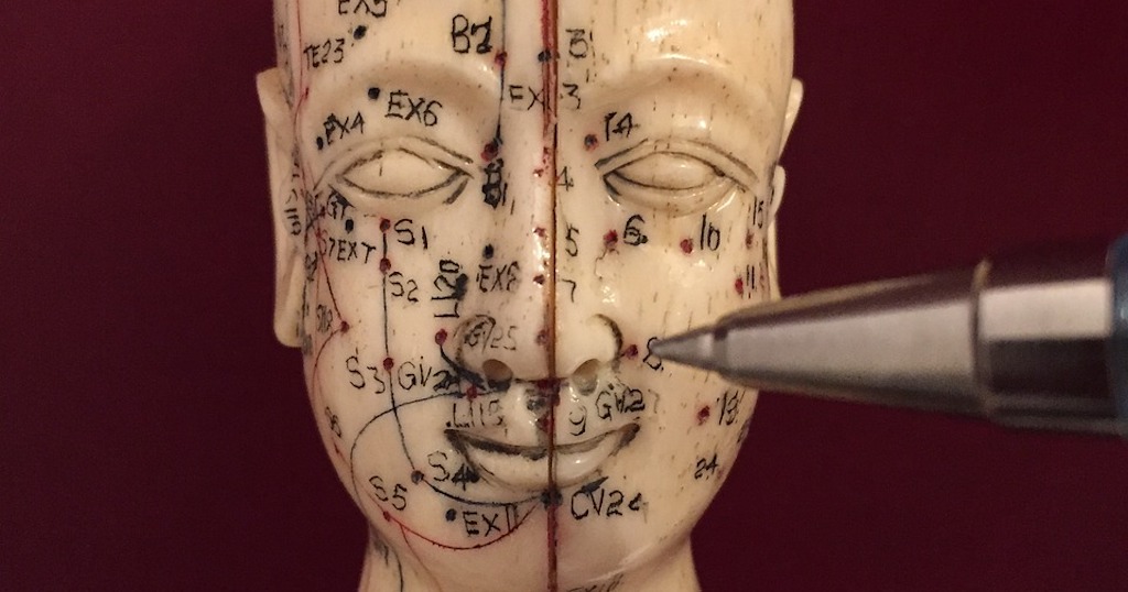 Diagrams of acupuncture points on an antique sculpture of a head.